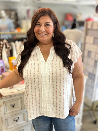 Woman wearing a white with pink flowers sleeveless blouse in a store setting