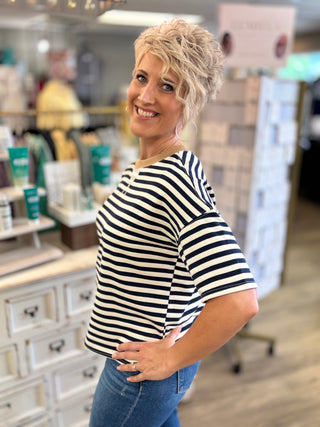 Model wearing white and navy striped top with tan collar trim