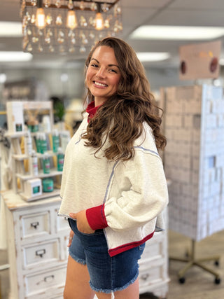 Model wearing an ash grey colored crew neck sweatshirt with contrast red ribbed collar and cuffs and blue stitching detail