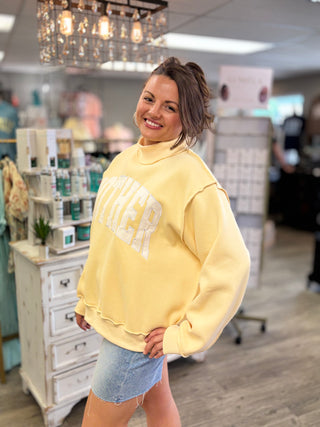 Model wearing butter yellow mock neck sweatshirt with ‘MOTHER’ embroidered on 