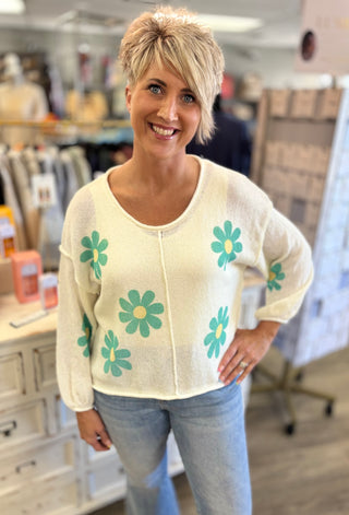 Woman wearing a white sweater with green floral patterns in an indoor setting