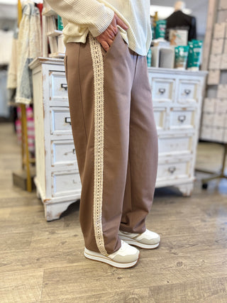 Model wearing mocha pants with cream lace detail.