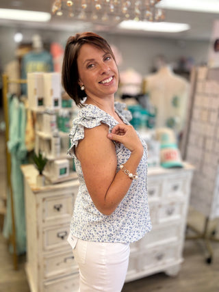Woman in a floral blouse and white pants standing in a clothing store.