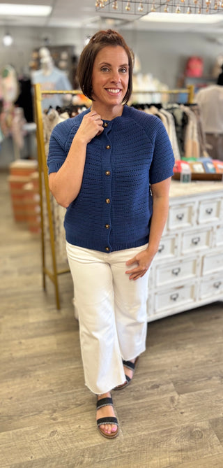 Woman wearing a blue button down cardigan and white pants in a clothing store.