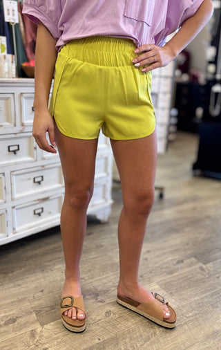Model wearing neon yellow shorts and a pink top in a store setting