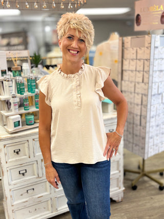Woman wearing a beige blouse with ruffled sleeves in a store setting