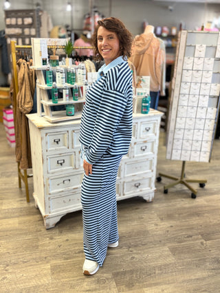A woman wearing a matching navy and light blue striped long-sleeve top and wide-leg pants set, standing in a retail store in front of a white wooden cabinet.