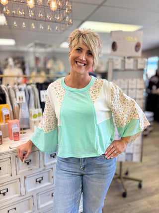 Woman wearing a light green top with patterned sleeves in a store setting