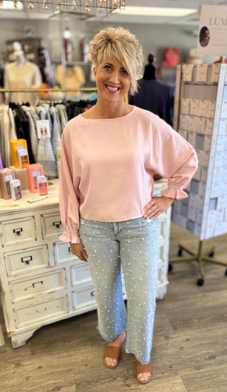 Woman wearing a light pink top and pearl and rhinestone studded jeans in a store setting