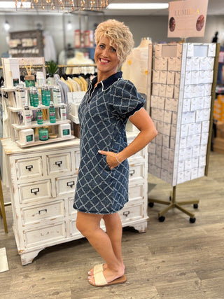 A woman modeling a short-sleeve collared mini dress with a blue and white geometric pattern, standing in a retail store setting.