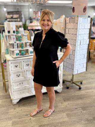 Woman in a black dress standing in a store with products and displays around her.