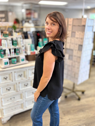 Model wearing a black top with ruffle detail and denim jeans