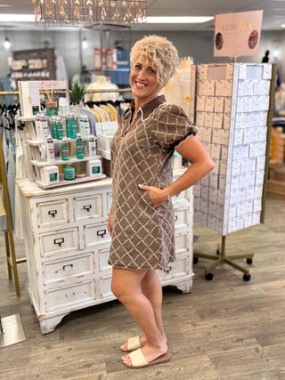 A woman modeling a brown and beige geometric print mini dress in a retail store setting.