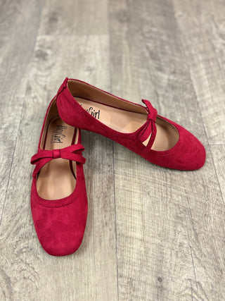 A pair of red suede ballet flats with bow details across the instep, displayed on a gray wood-look floor.