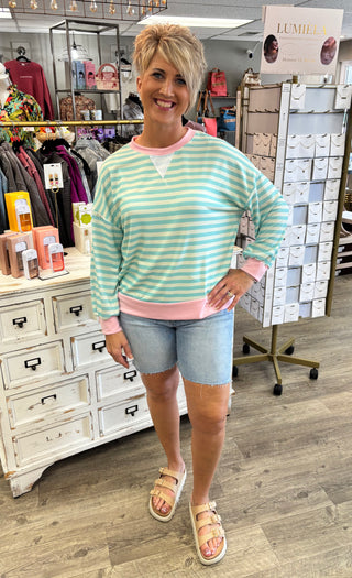 Model wearing mint green striped top and light wash, longer length denim shorts with raw hem.