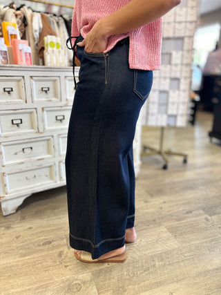 Person wearing dark denim wide leg  jeans and a pink top in a store setting