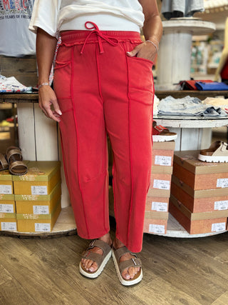 Model wearing red barrel fit sweat pants with exposed stitching, pockets, and drawstring detail