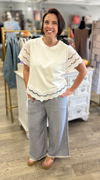 Woman wearing a white lace-trimmed top and light blue pants in a store setting