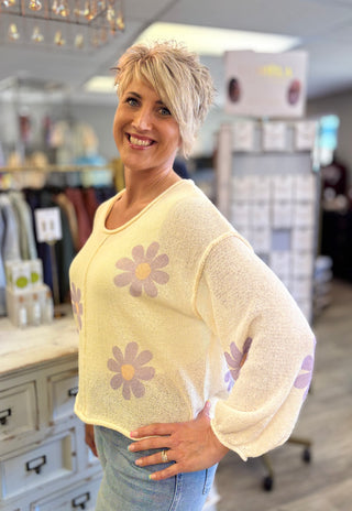 Woman wearing a cream sweater with lavender floral patterns in a store setting
