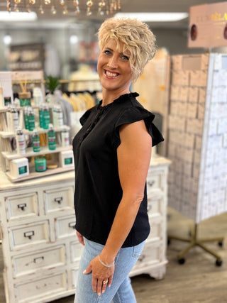 Woman in a black top and jeans standing in a store with shelves and products in the background.