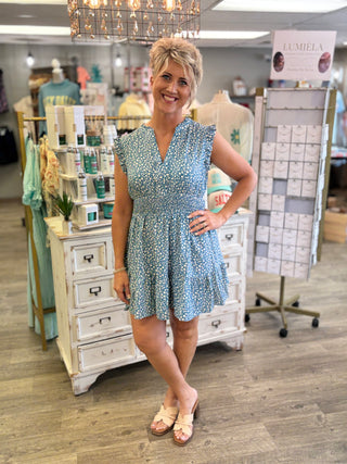 Woman in a blue dress standing in a store with furniture and decor items.