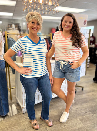 Two women posing in a store wearing striped shirts and jeans/shorts.