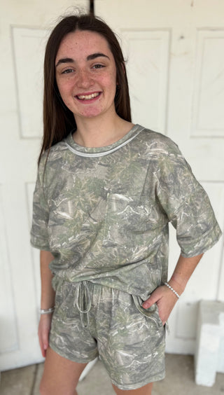 Model wearing a camouflage shorts set with a white background