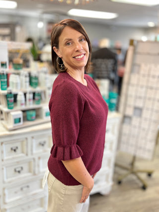 Model wearing a burgundy sweater with ruffle detail