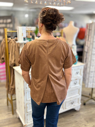 Back view of the camel Salted Caramel Suede Top showing the button keyhole closure and pleated split back hem, styled with dark jeans