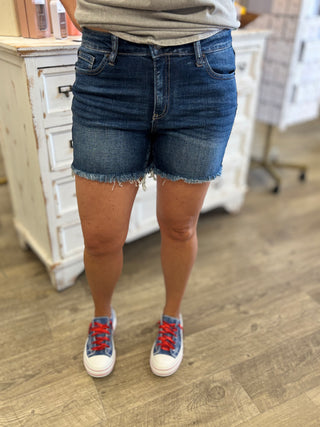 Person wearing blue denim shorts and sneakers on a wooden floor.