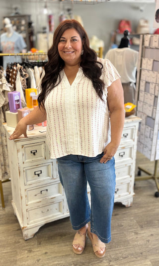 Woman in a white with pink flowers sleeveless blouse and blue jeans standing in a store setting.