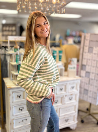 Model wearing a green and cream striped sweater with red stitching detail and jeans