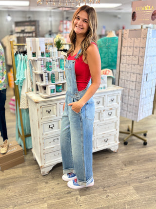 Woman wearing a red tank top and blue overalls standing in a store.