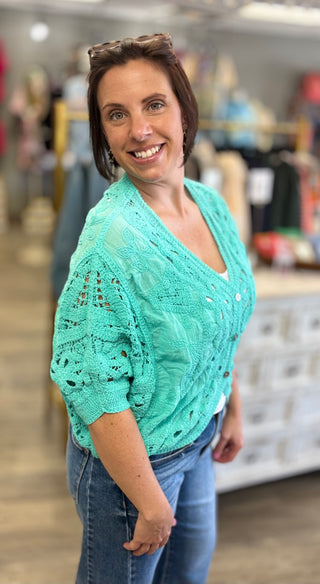 Woman wearing a short sleeve mint crocheted cardigan in a store setting