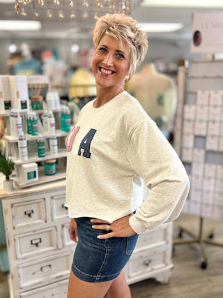 Model wearing cream sweatshirt with ‘USA’ in red, white, and blue letters