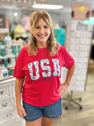 Woman wearing a red 'USA' t-shirt with floral letters in a store setting