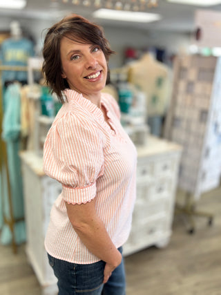 Model wearing peach and white striped blouse in a store setting 