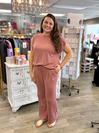 Woman in a brick red outfit standing in a store with clothing racks and displays in the background.