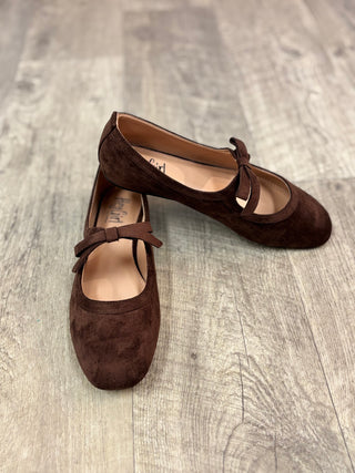 A pair of dark brown suede ballet flats with bow details, displayed on a gray wood-look floor.