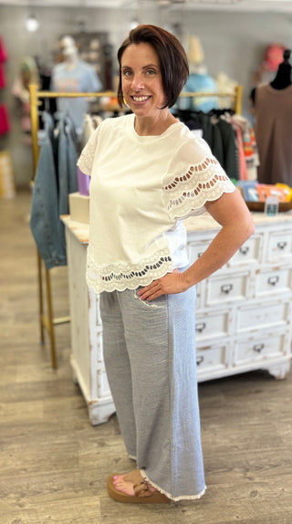 Woman wearing a white blouse with lace details and light blue pants in a clothing store.