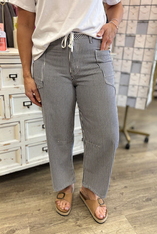 Person wearing striped pants and a white shirt in a room with a dresser and patterned wall.