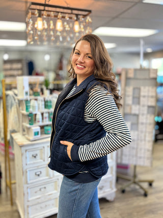 Model wearing a navy quilted vest with a navy and white long sleeve top and jeans.