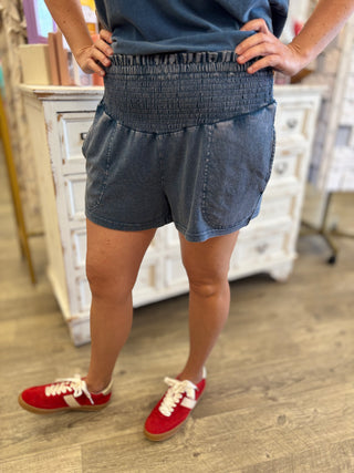 Person wearing blue shorts and red sneakers in a room with wooden flooring and white furniture.