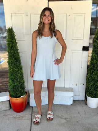 Woman in a light blue dress standing in front of a white door with plants on either side.