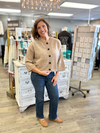 Model wearing the Halfway There Knit Cardigan Sweater in soft mocha with chocolate brown buttons, styled with dark straight-leg jeans and tan loafers
