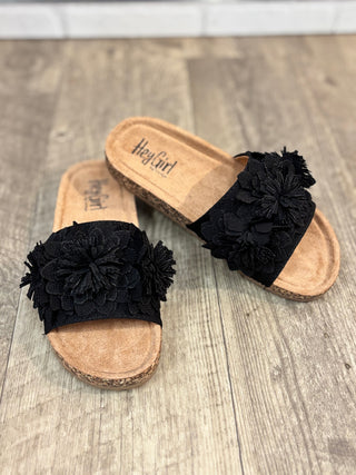 Black floral sandals with cork soles on a wooden floor, featuring 'Hey Girl' branding.