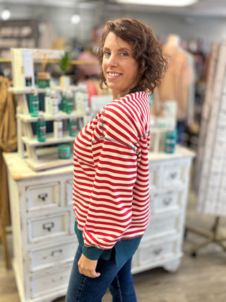 A woman with short brown curly hair wearing a red and white striped long-sleeve top and blue jeans, posing in a retail store setting.
