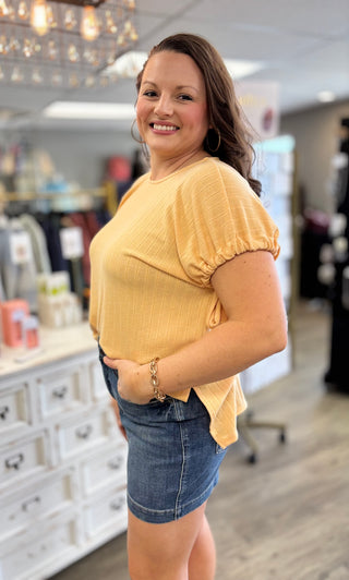 Woman wearing a yellow top and denim shorts in a store setting