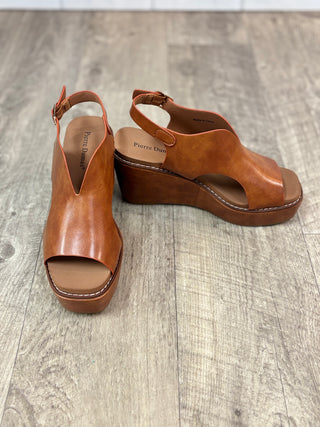 A pair of women's brown leather wedge sandals with open toes and ankle straps, displayed on a gray wood-look floor. The brand name 'Pierre Dumas' is visible on the insole.