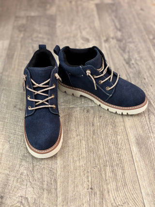A pair of navy blue suede ankle boots with beige laces and white soles, displayed on a light brown wood floor.
